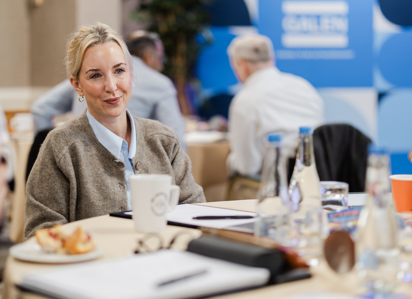 Woman smiling at a conference table during a professional meeting, with water bottles and notebooks in the foreground