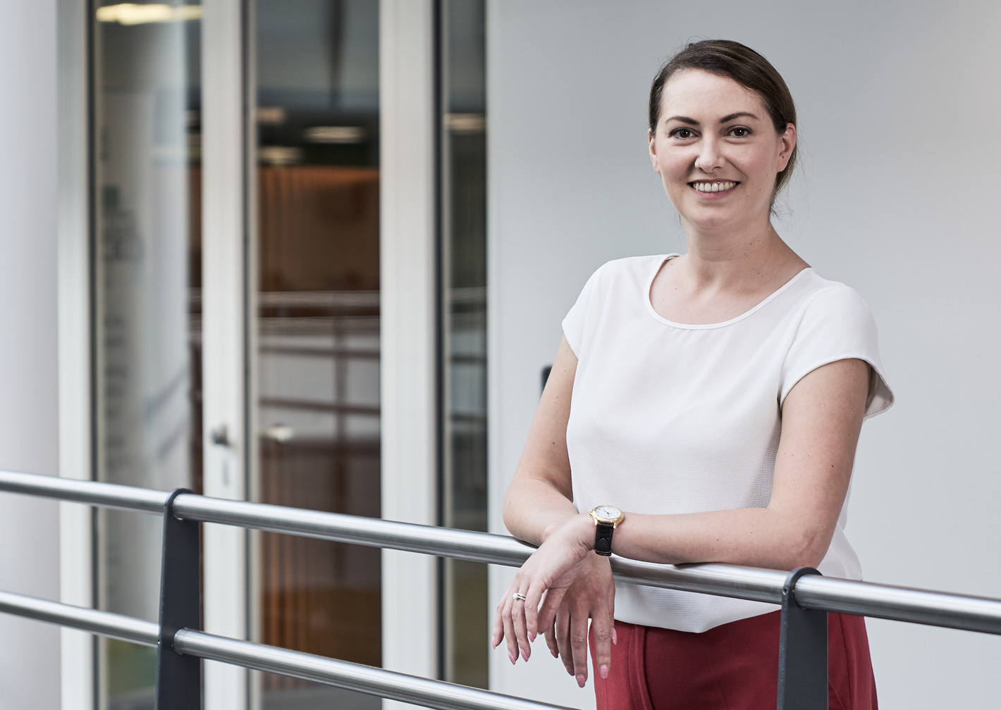 Smiling woman in a white top leaning on a railing in a modern office building