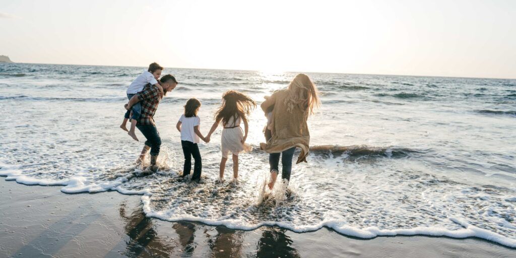 Familie mit drei Kindern läuft bei Sonnenuntergang durch die Brandung am Strand.