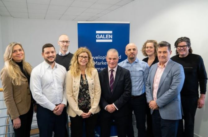 Group of nine professionals posing together in front of a Galen branded banner following acquisition announcement