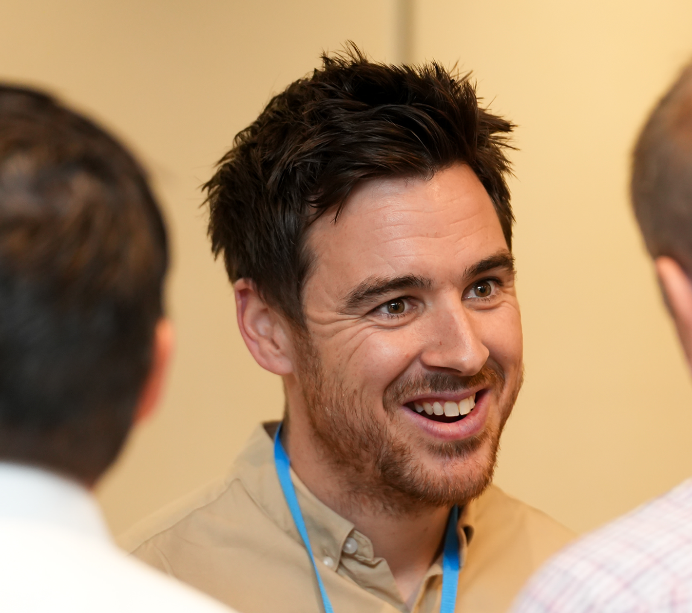 Smiling man with a blue lanyard engaged in conversation with colleagues at a professional networking event