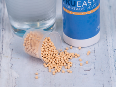PKU EASY Microtabs Plus supplement pearls pouring from a measuring spoon next to a glass of water
