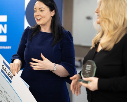 Two women at a Galen award ceremony, one holding a large cheque and the other holding a glass trophy