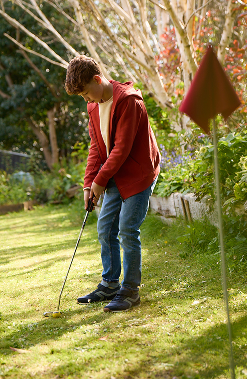 A teenage boy playing mini-golf in a sunny garden