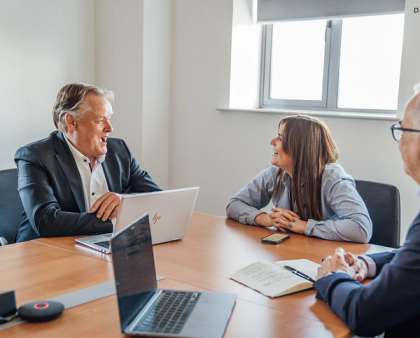 Three colleagues engaged in a business meeting around a conference table with laptops and notebooks