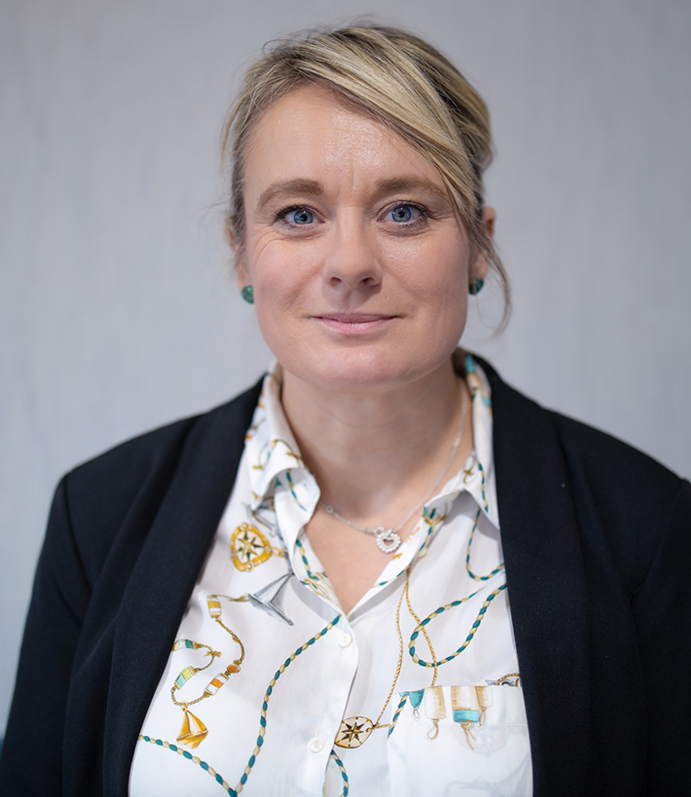Laura Mustalahti - woman with short blonde hair, dark blazer over patterned blouse