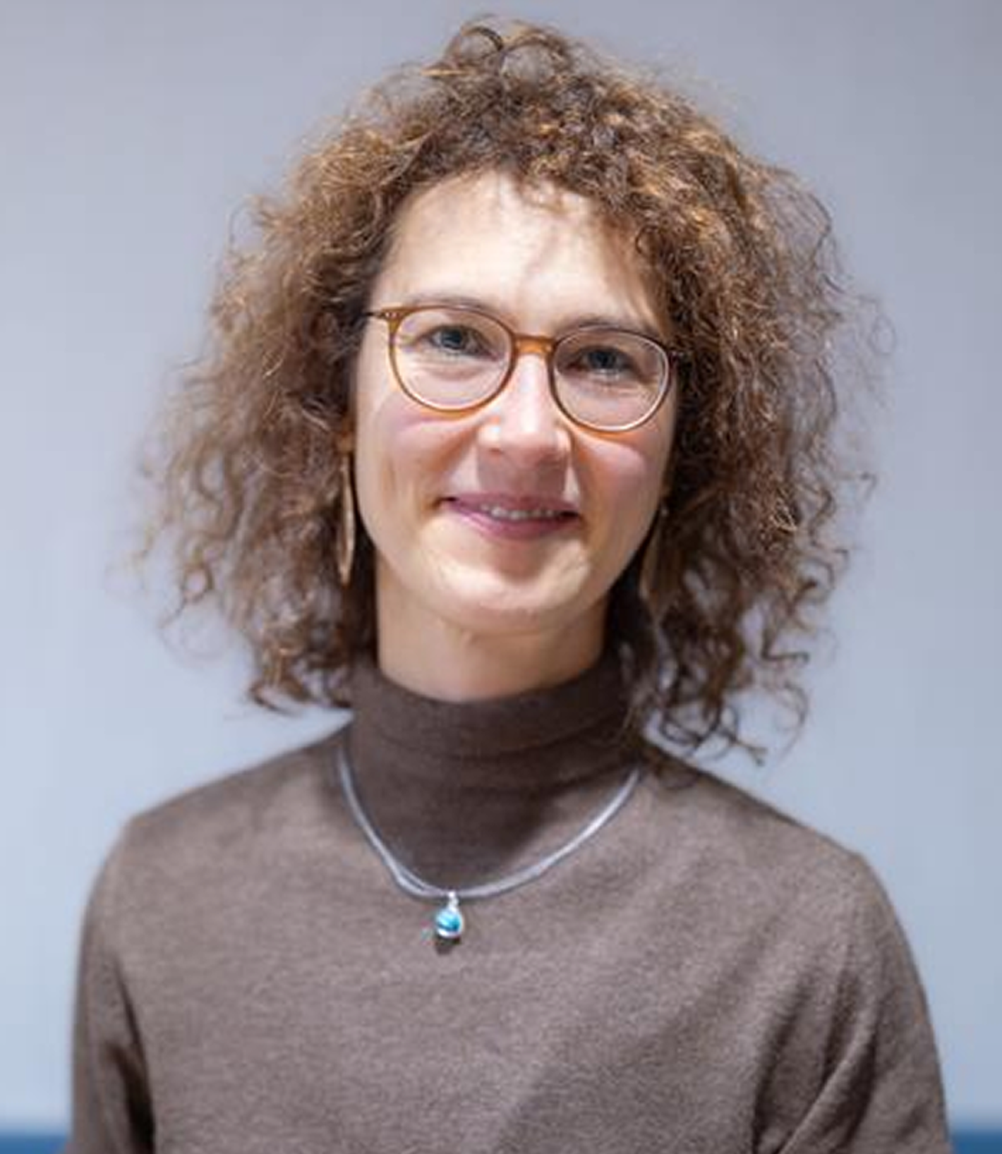Juliane Schlothauer - woman with curly hair and glasses, brown sweater