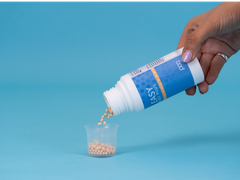 Hand pours beige supplement pellets from a blue Easy Poo bottle into a small plastic measuring cup