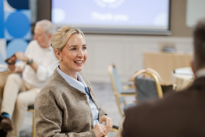 Smiling woman in a tan cardigan engaged in conversation at a professional conference or seminar