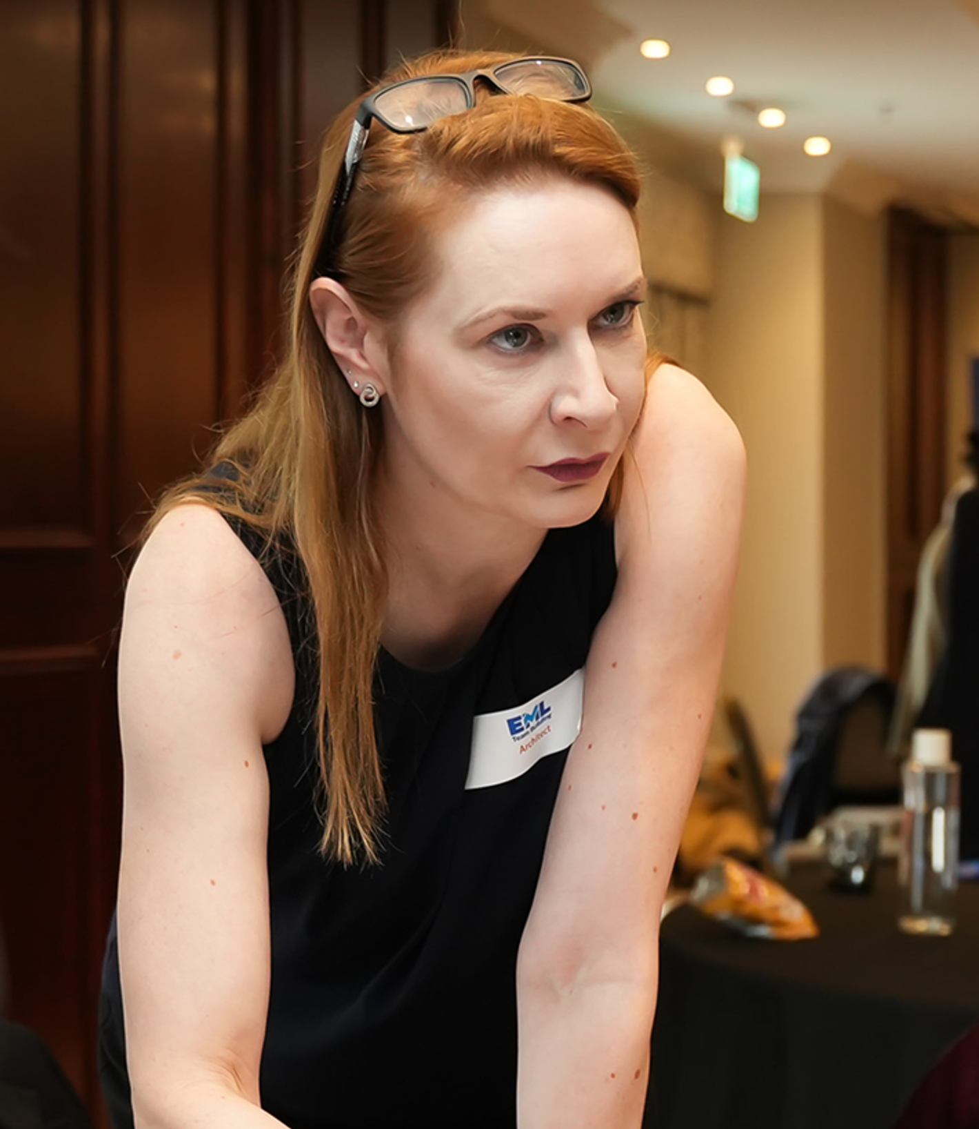 Kirsten Beusse - woman with red hair, sleeveless dark top, warm-lit interior