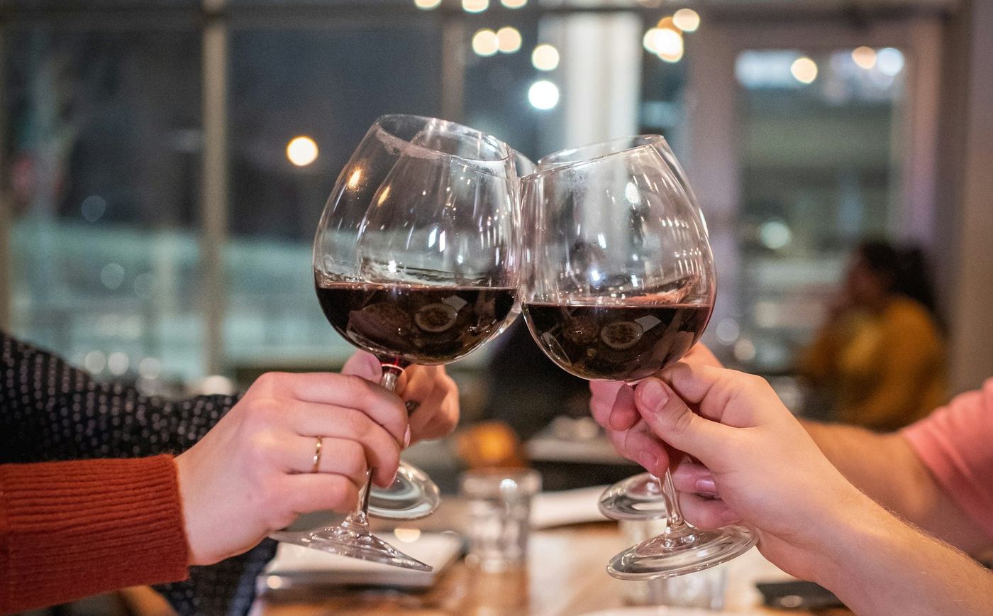 Zwei Gäste stoßen am Tisch mit Rotwein an
