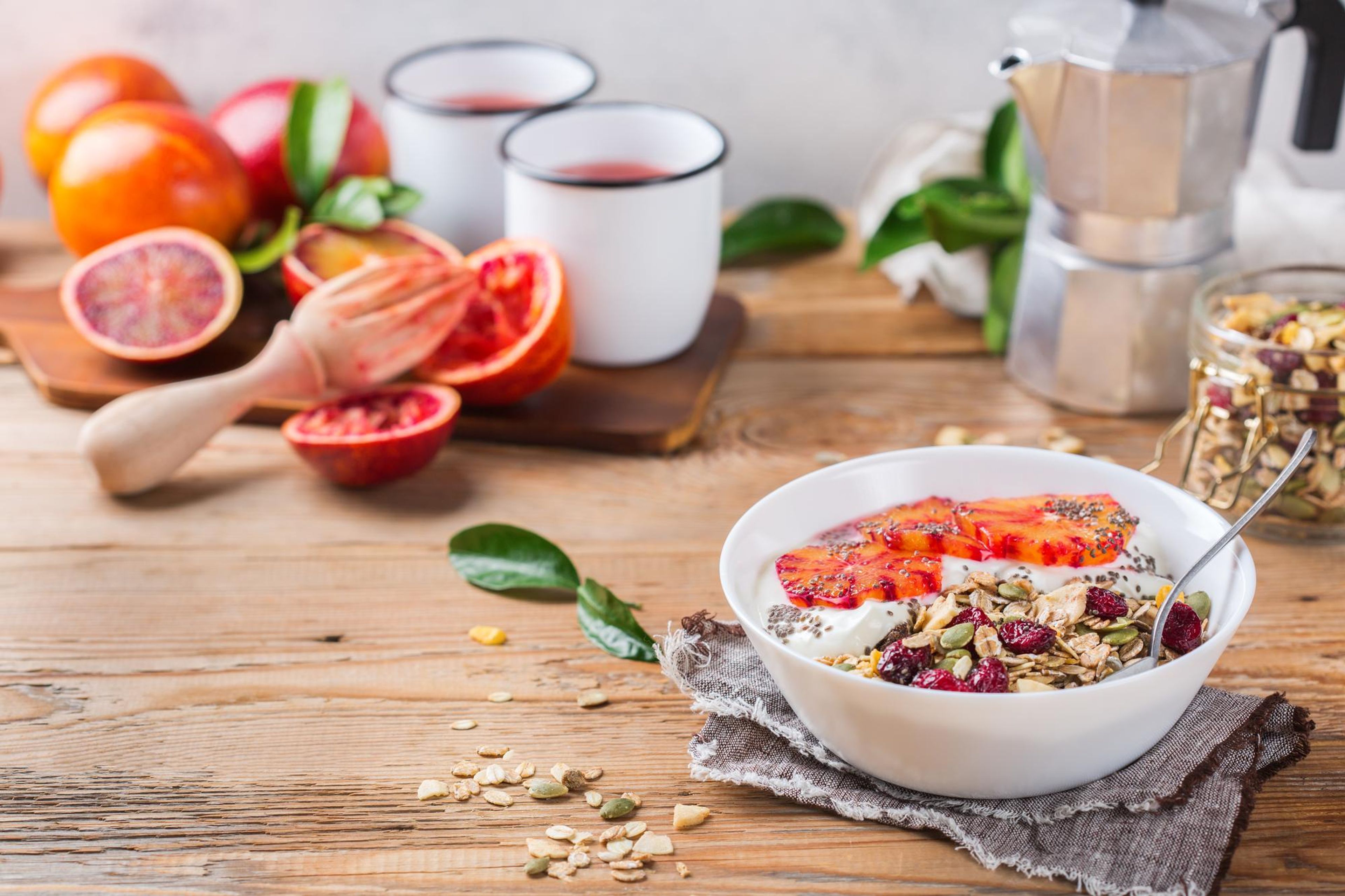 Breakfast with yogurt, blood oranges, granola, and coffee on a wooden table.