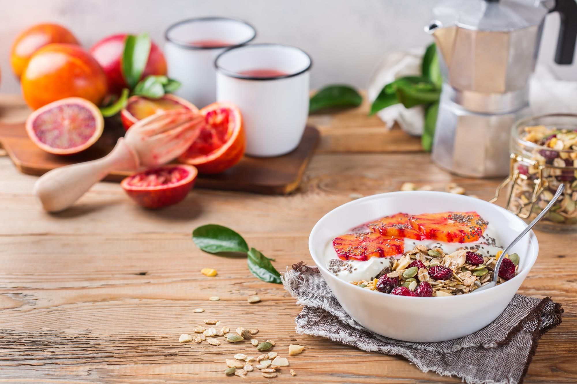 Breakfast with yogurt, blood oranges, granola, and coffee on a wooden table.