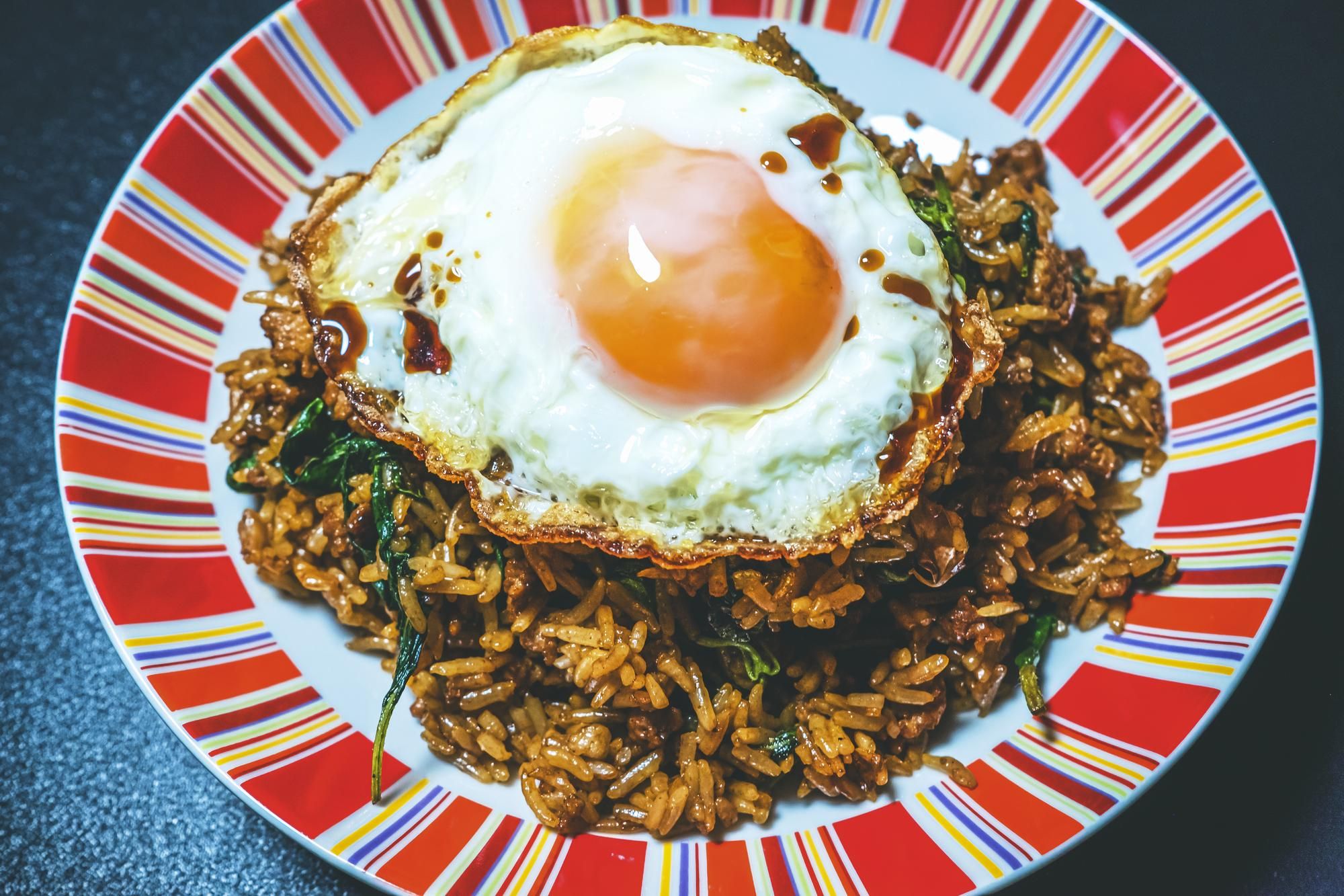 Basil fried rice topped with a fried egg and sauce on a striped plate.