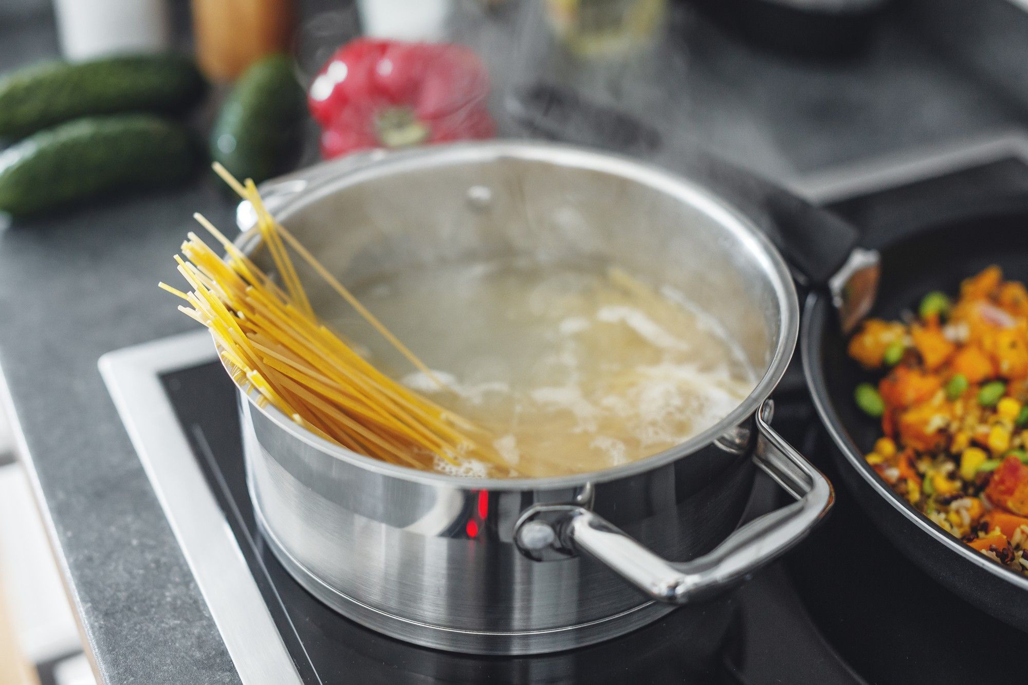 A pot of boiling spaghetti and a pan of vegetables cooking on a stove.