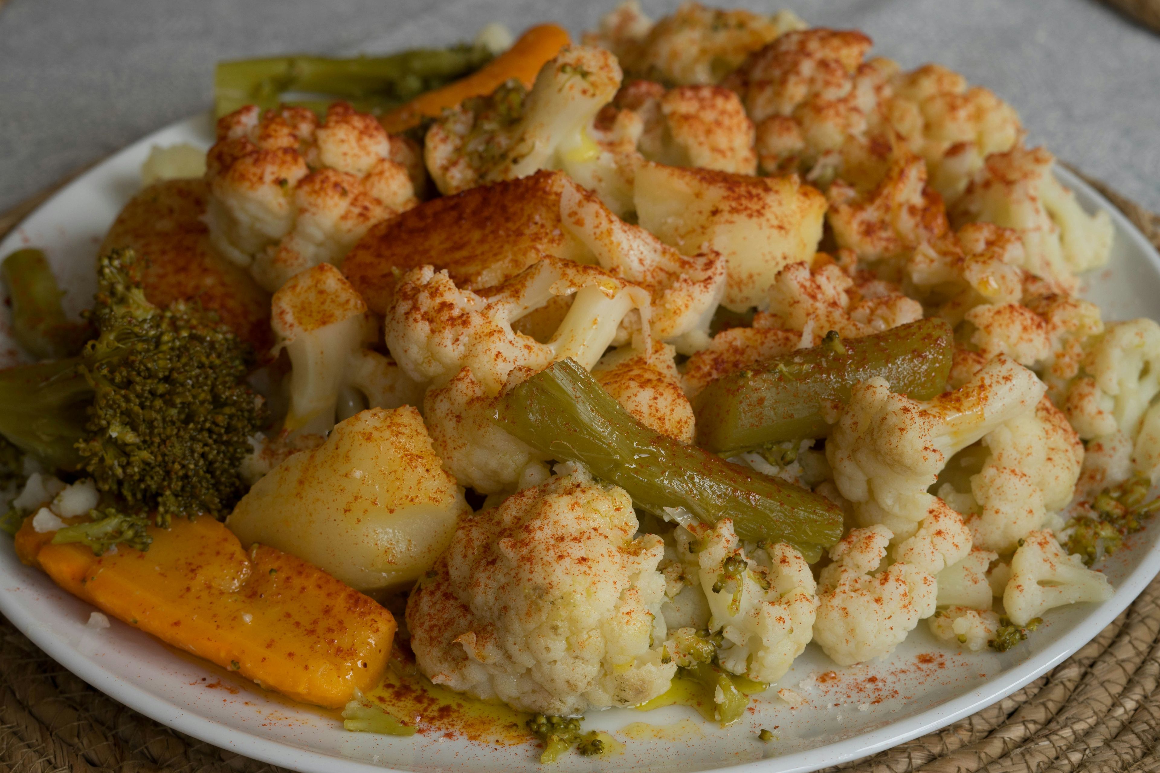 Cooked cauliflower, potatoes, broccoli, green beans, and orange bell pepper on a plate, seasoned with paprika.