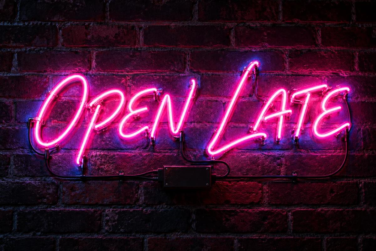 Pink OPEN LATE neon sign on a dark brick wall