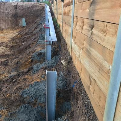 Galvanised steel retaining wall posts concreted into staged excavation bays beside a timber boundary fence