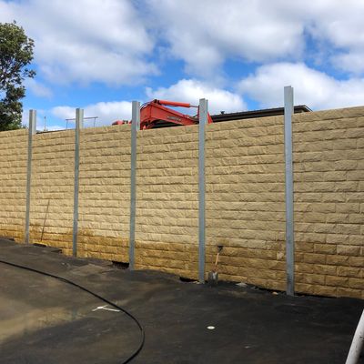 Tall sandstone block-finish retaining wall with galvanised steel posts beside a townhouse carpark