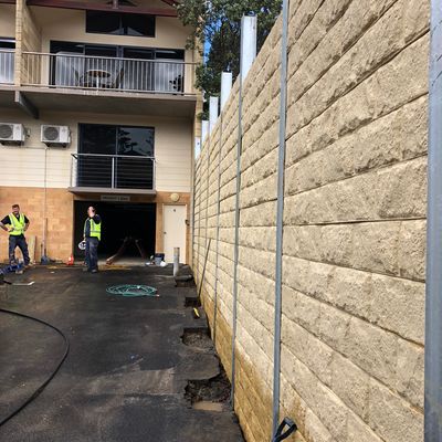 High block-finish concrete sleeper retaining wall under construction between townhouses and a carpark driveway