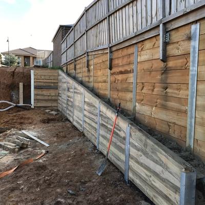 Near-complete timber sleeper retaining wall built in stages below an existing boundary fence, Geelong region