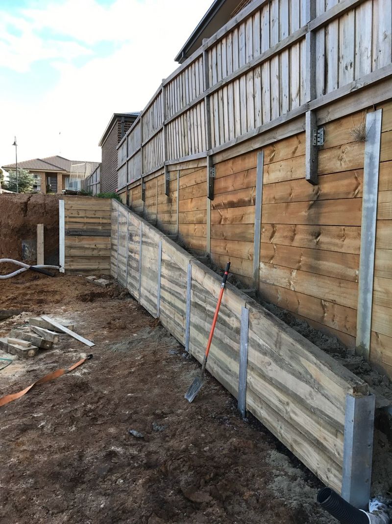 Completed timber sleeper retaining wall built in stages directly below a boundary fence