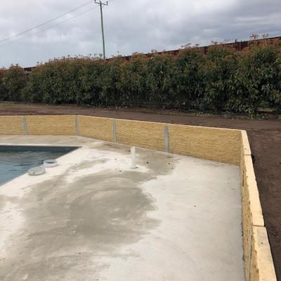 Stackstone-finish concrete sleeper retaining wall around a new swimming pool and concrete surround on a rural block