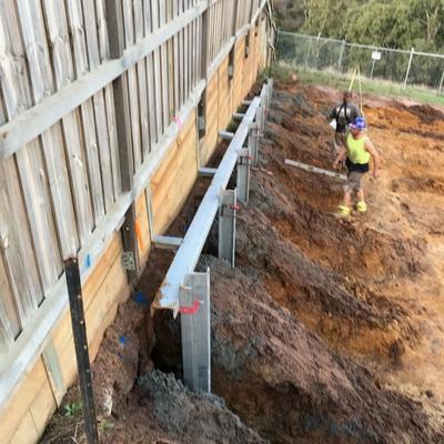 Retaining wall posts and walers installed in stages along a steep boundary above a reserve, protecting the fence line above