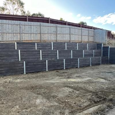 Stepped dark sleeper retaining walls terracing a slope below residential fences, Geelong region