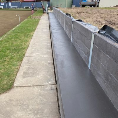 Tiered concrete spectator seating built on a retaining wall alongside the bowling green at Belmont Bowling Club