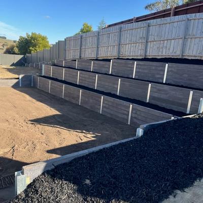 Finished three-tier dark timber sleeper terraced retaining walls with fresh mulch garden beds on a sloping block
