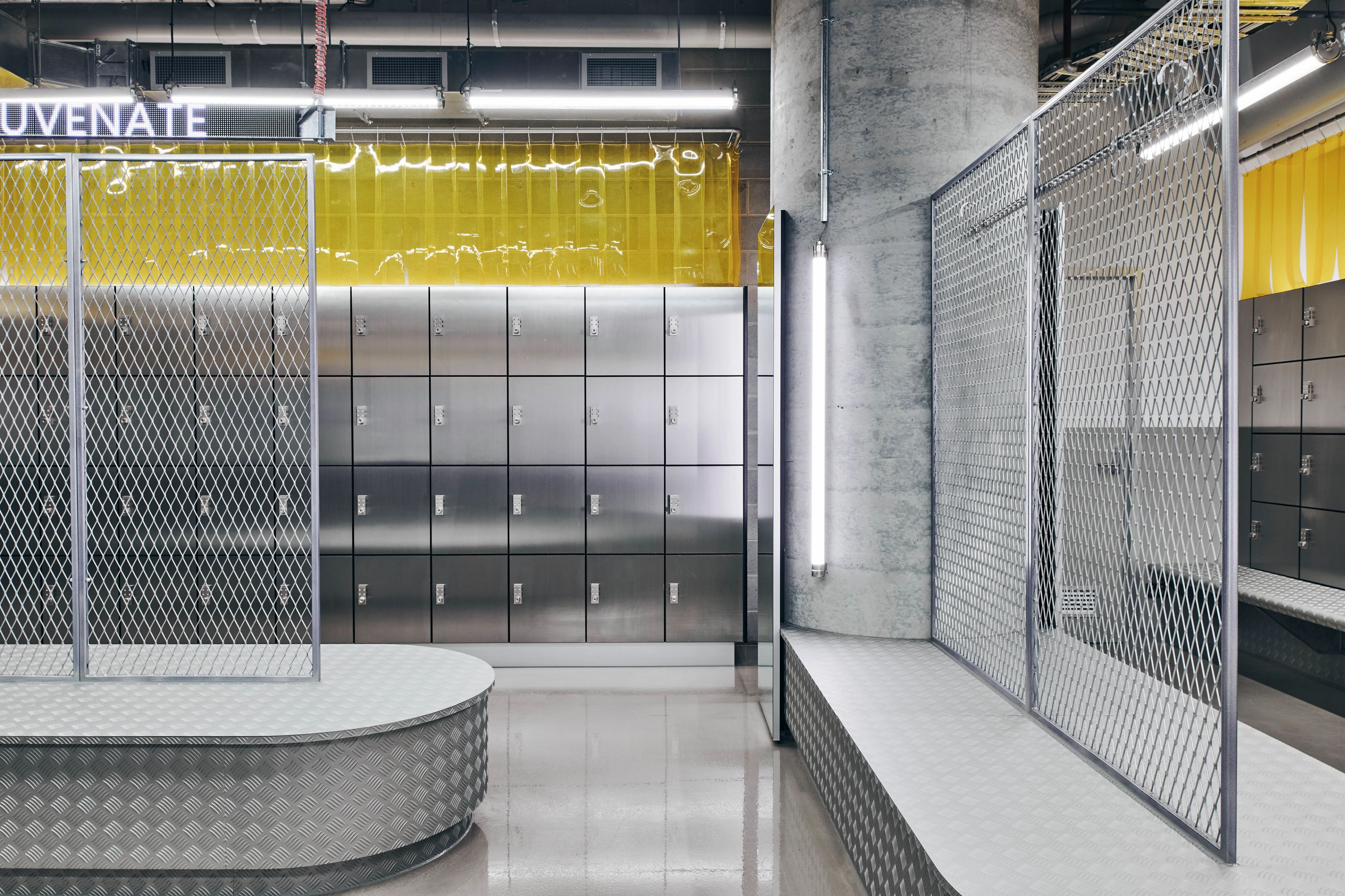 A stainless steel clad locker room at 1R Australia by Foolscap. The techno-gym offers industrial showers and locker rooms complete with butchers curtains, raw concrete, and exposed lighting, inspired by the idea of stitching yourself back together after a tough workout.