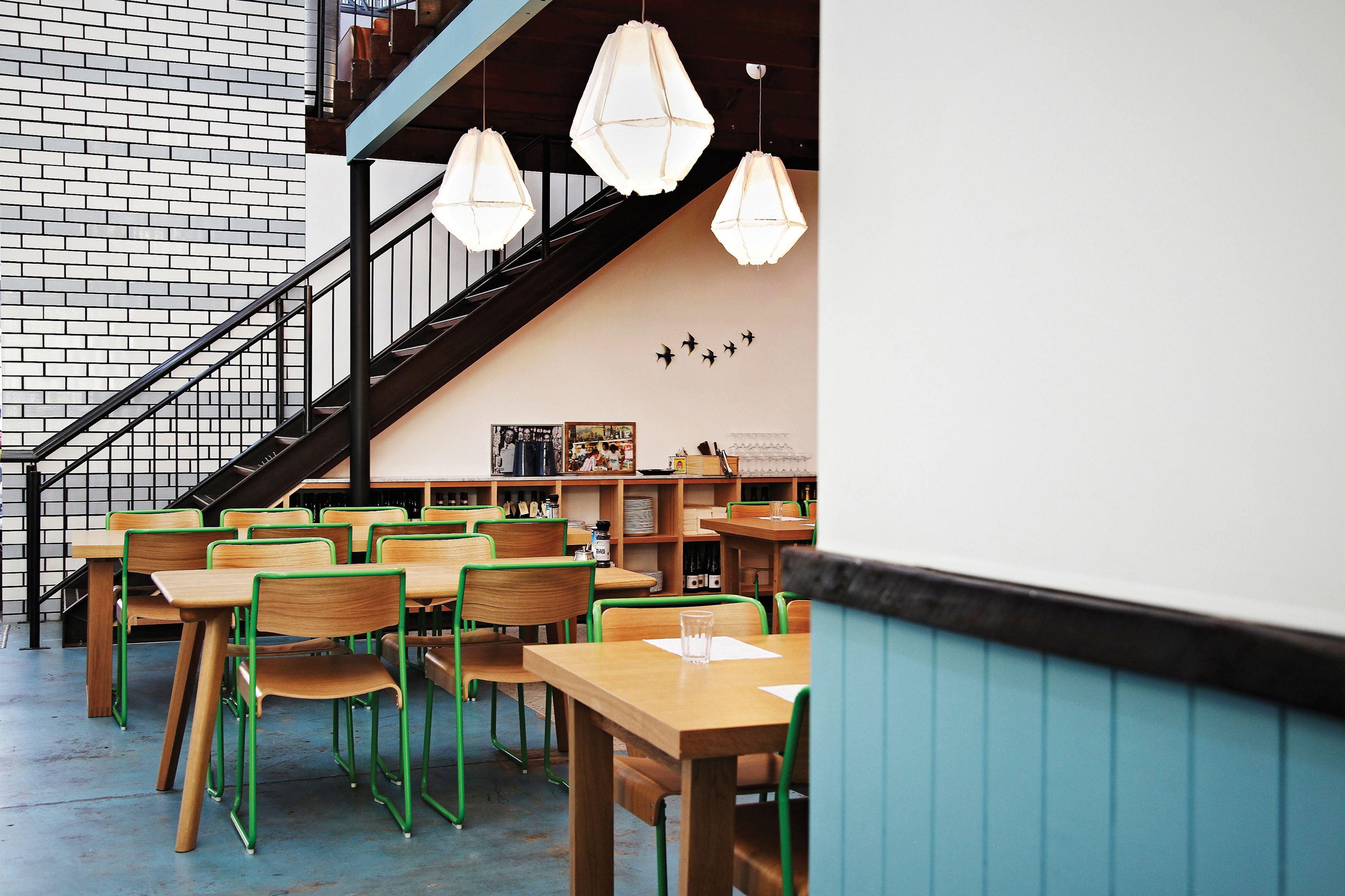 Gordon Street Garage, designed by Foolscap. Stairs to a mezzanine can be seen behind timber chairs and tables with green steel accents.