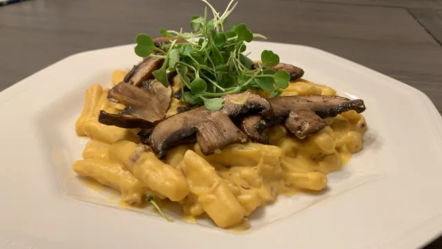 Creamy pumpkin pasta topped with sautéed mushrooms and fresh microgreens on a white plate.
