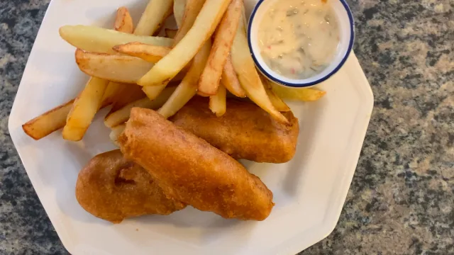 Golden beer-battered fish and chips served on a white plate with tartar sauce in a small bowl.