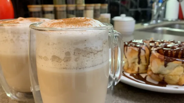 French vanilla cappuccino with cinnamon foam in glass mugs, pastries with chocolate drizzle in background.