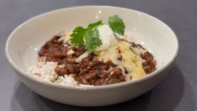 Vegetarian chili served in a white bowl with white rice, topped with sour cream and fresh cilantro.