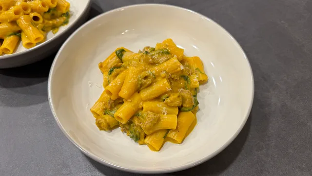 Creamy butternut squash sausage pasta with rigatoni noodles and green herbs in a white bowl.