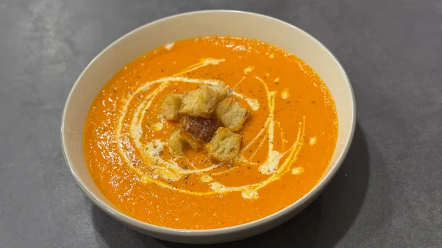 Creamy roasted tomato soup in a white bowl, garnished with croutons and a drizzle of cream.