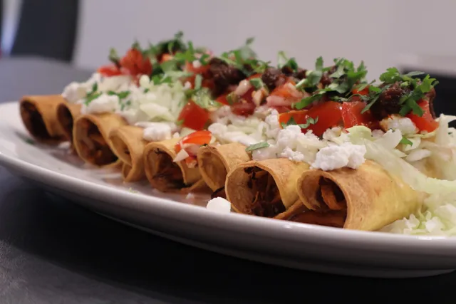 Crispy air fryer taquitos rolled in golden tortillas, topped with shredded cheese, diced tomatoes, and fresh cilantro on a white plate.