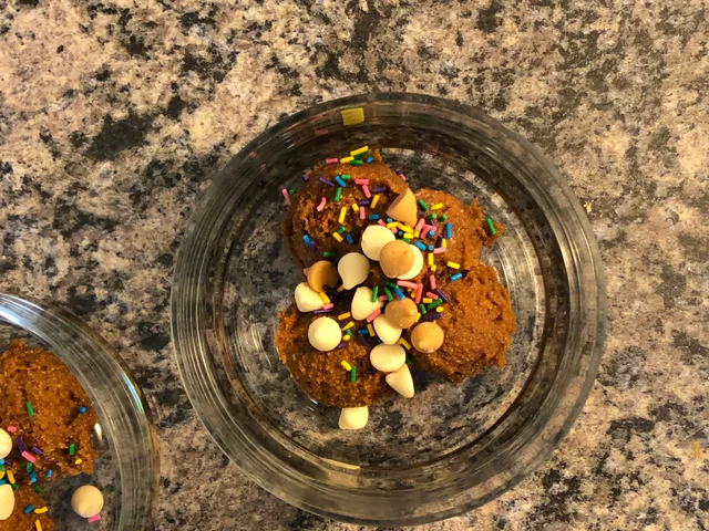Edible pumpkin cookie dough in a glass bowl topped with white chocolate chips and colorful sprinkles.