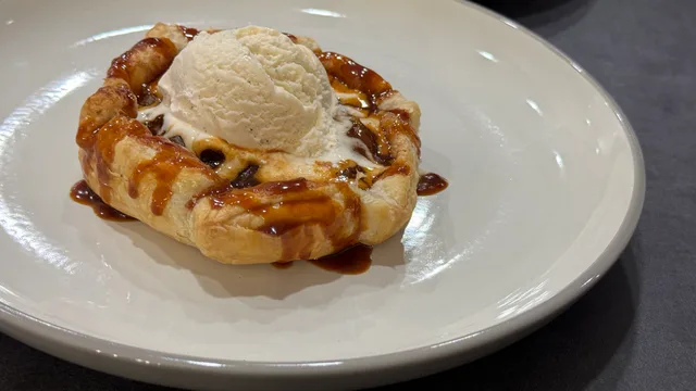 Mini puff pastry apple pie topped with vanilla ice cream and caramel drizzle on a white plate.