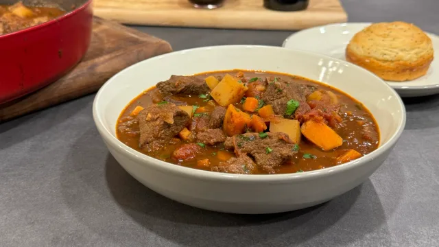 Hearty Portuguese beef stew with tender meat, potatoes, and carrots in rich brown gravy, served in a white bowl with crusty bread.