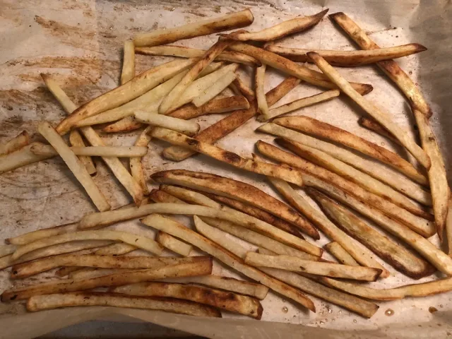 Crispy oven-baked fries with golden-brown exterior spread on parchment paper.