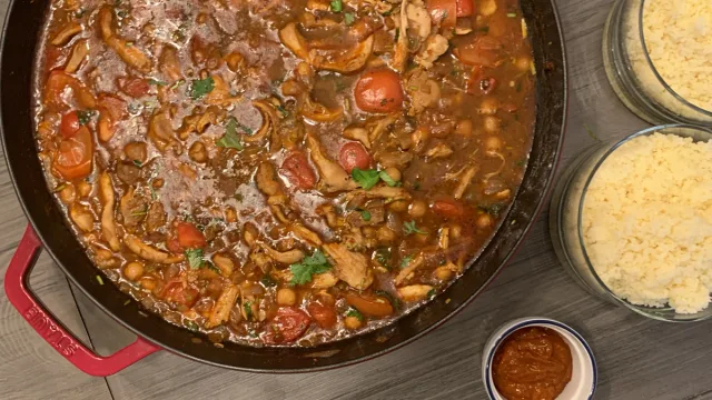 One-pot Moroccan chicken and chickpea stew in a red Dutch oven with couscous and sauce on the side.