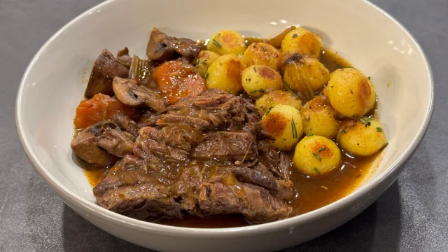 Tender pot roast with mushrooms and roasted golden potatoes in rich brown gravy, served in a white bowl.