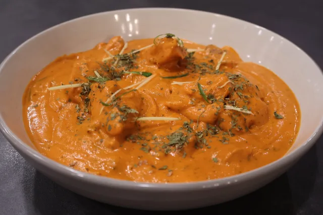 Murgh Makhani served in a white bowl with creamy tomato sauce, topped with fresh herbs and sliced almonds.