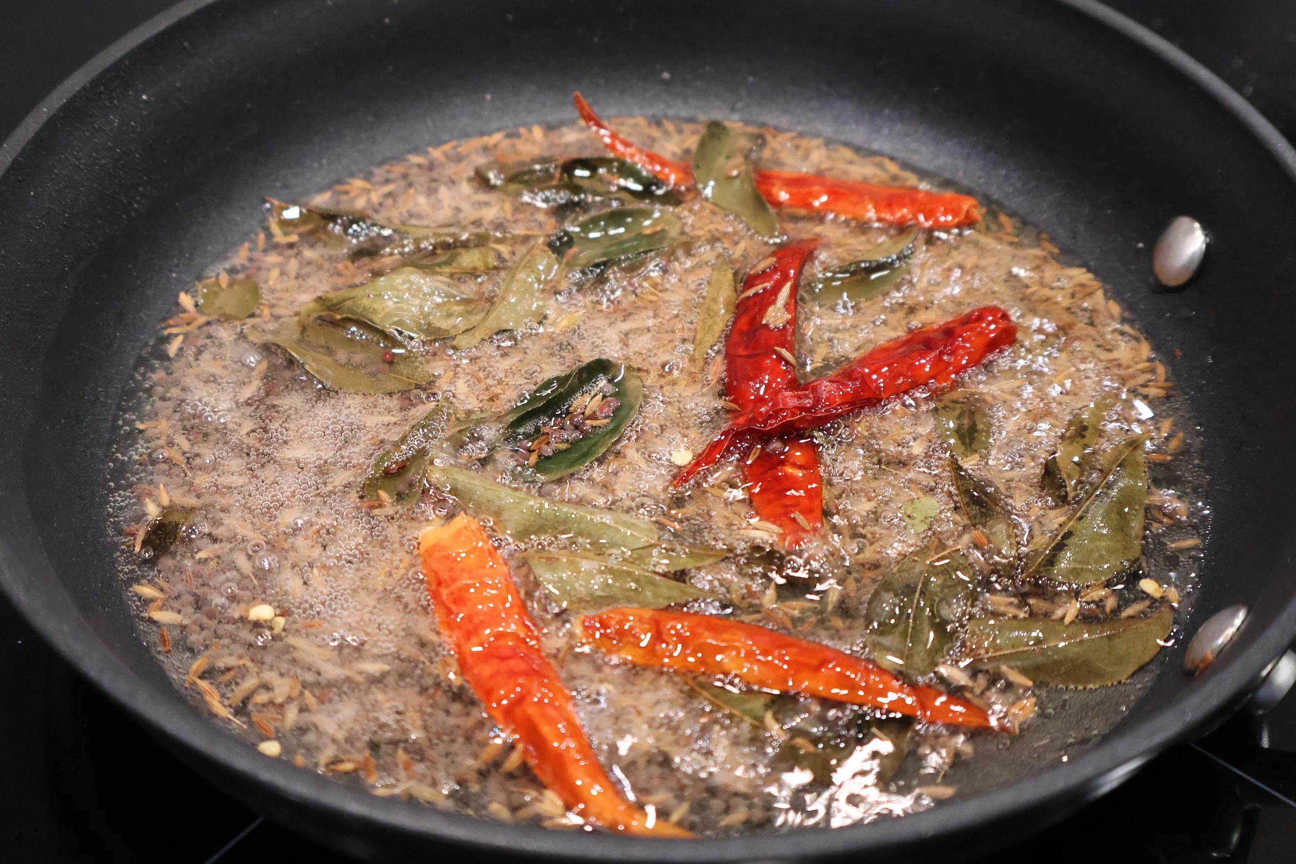 Tadka blooming in a dark pan: whole green and red chilies sizzling in hot oil and spices.