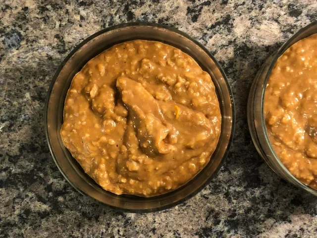 Two round baking pans filled with thick, golden-brown pumpkin oatmeal mixture on granite countertop.