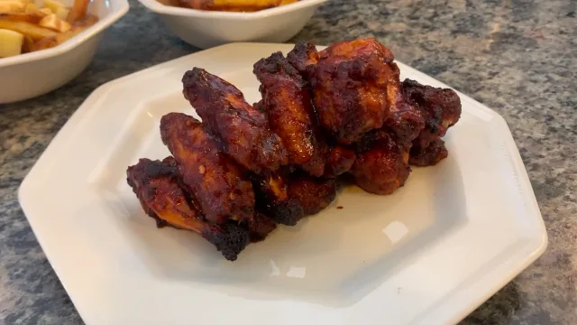 Glazed spicy BBQ chicken wings on a white plate with crispy, caramelized edges and dark char marks